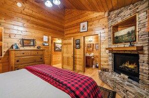 Ein rustikales Blockhaus-Interieur mit Kamin, Holzwänden, einem Bett mit kariertem Überwurf und einer Kommode.