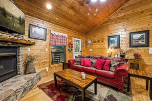 Ein gemütliches Blockhaus-Interieur mit Kamin aus Stein, Holzwänden, einer roten Ledersofa und gerahmten Bildern.