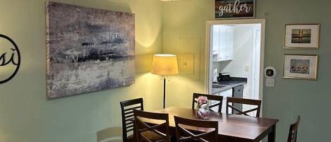 A dining area with a table and chairs, a lamp, and a wall with a 'gather' sign.