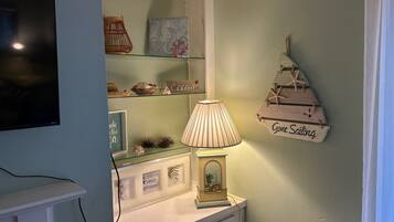 A room with a television mounted on the wall, a lamp on a table, and a shelf with decorative items.