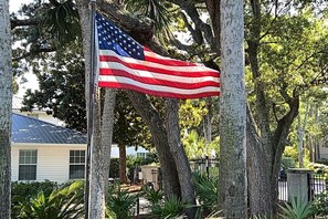 Amerikan lippu on kiinnitetty lipputankoon asuinalueella, jossa on puita ja taustalla näkyy talo.