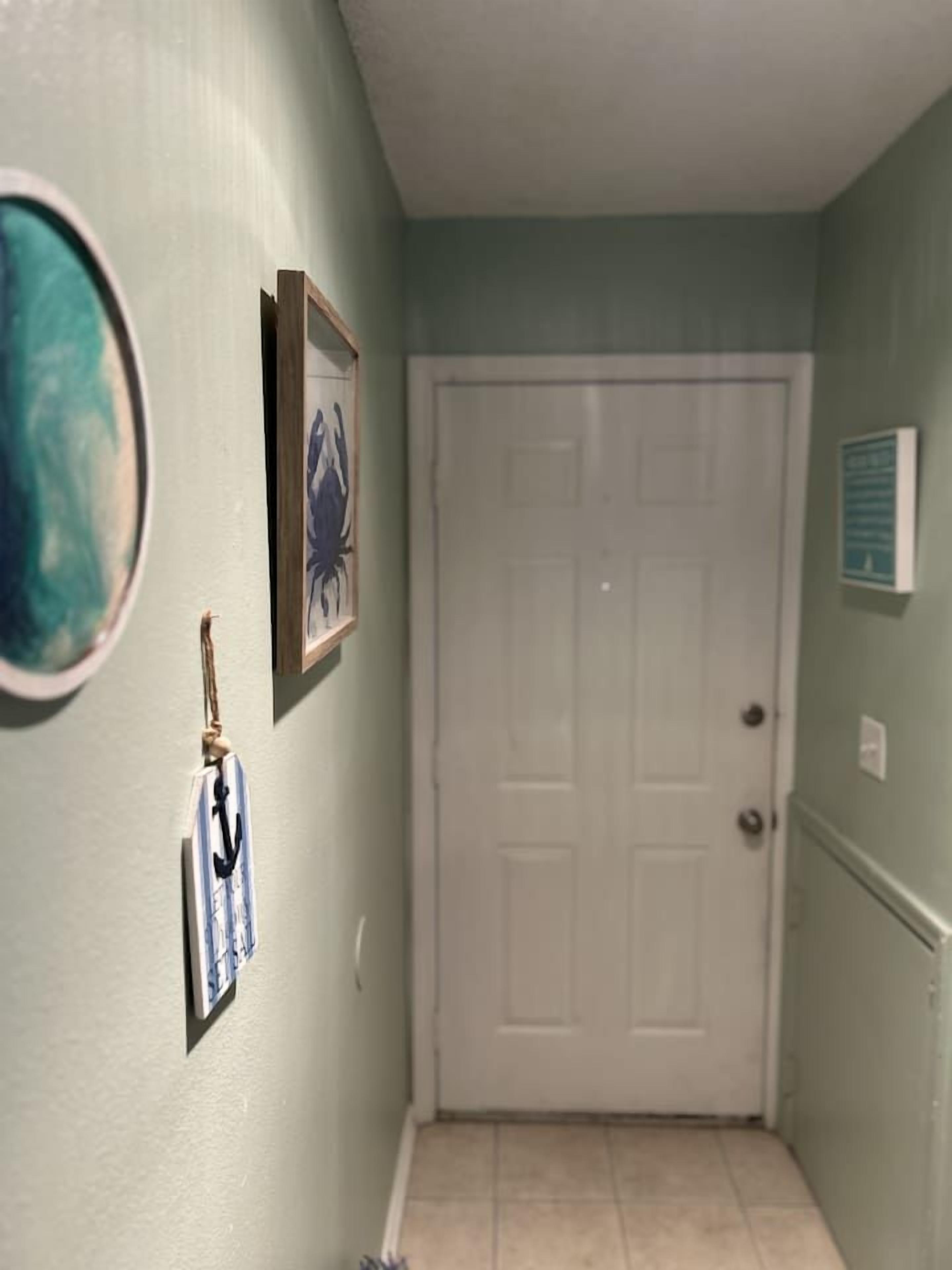 Un pasillo con una puerta blanca, un cuadro enmarcado y un adorno colgado en la pared.