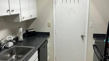 A compact kitchen with a sink, cabinets, a door with hooks, and a stove.