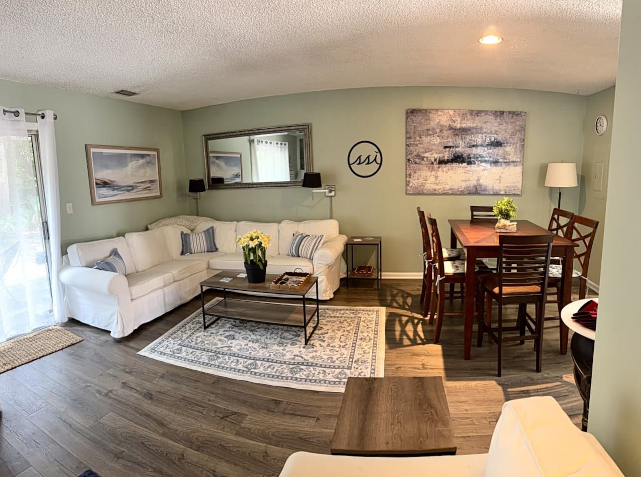 A living room with a sectional sofa, a coffee table, a dining table with chairs, and a rug.