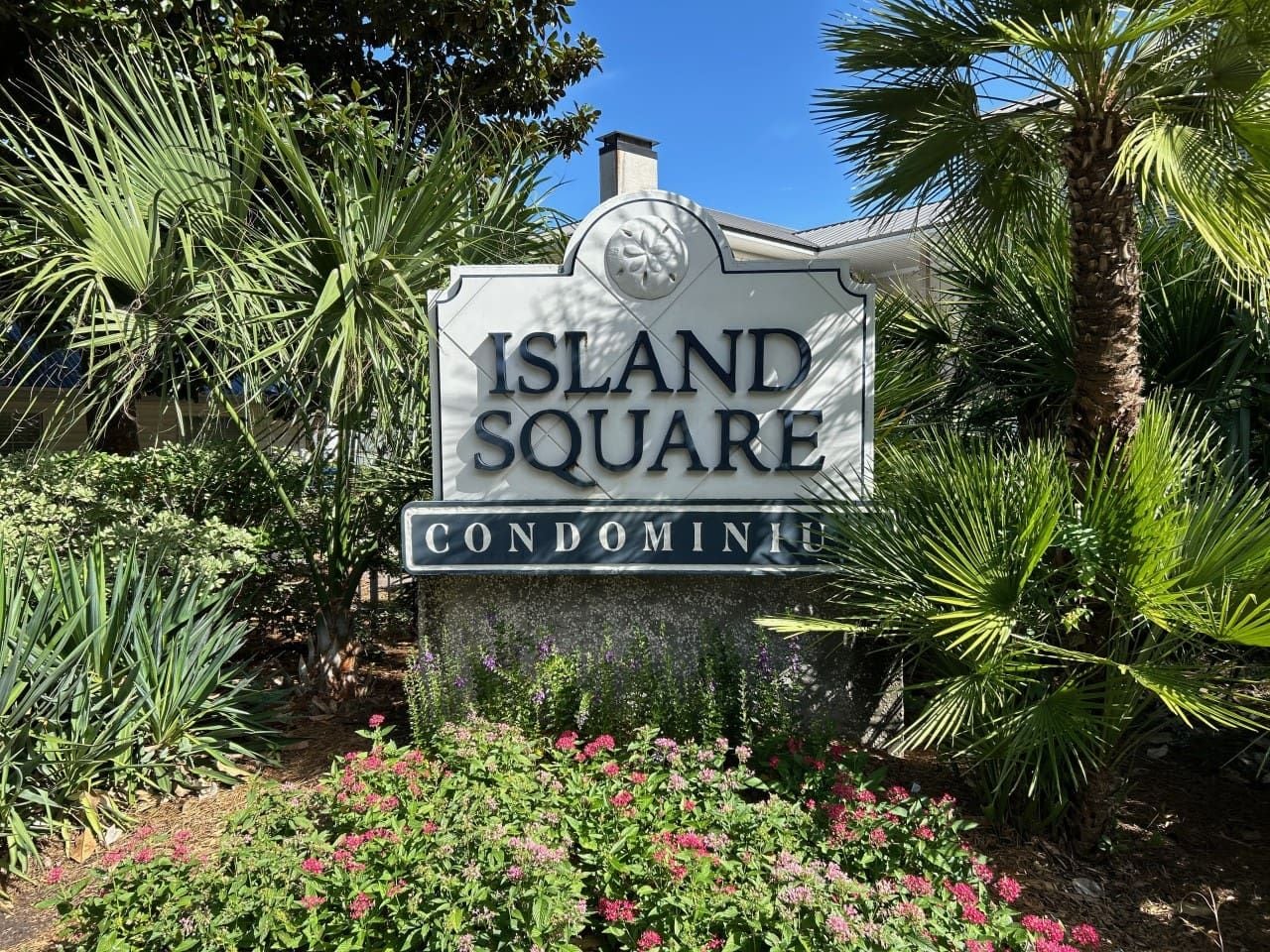 A sign for 'Island Square Condominium' surrounded by tropical plants and flowers.
