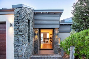 Ein modernes Haus mit einer Stein-Fassade, einer Holzdielen-Terrasse und Blick ins Innere.