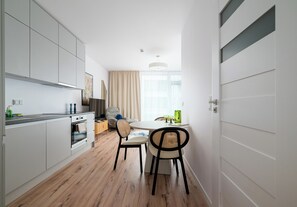 Een moderne keuken met een inbouwoven, een eethoek met tafel en stoelen, en een groot raam met gordijnen.