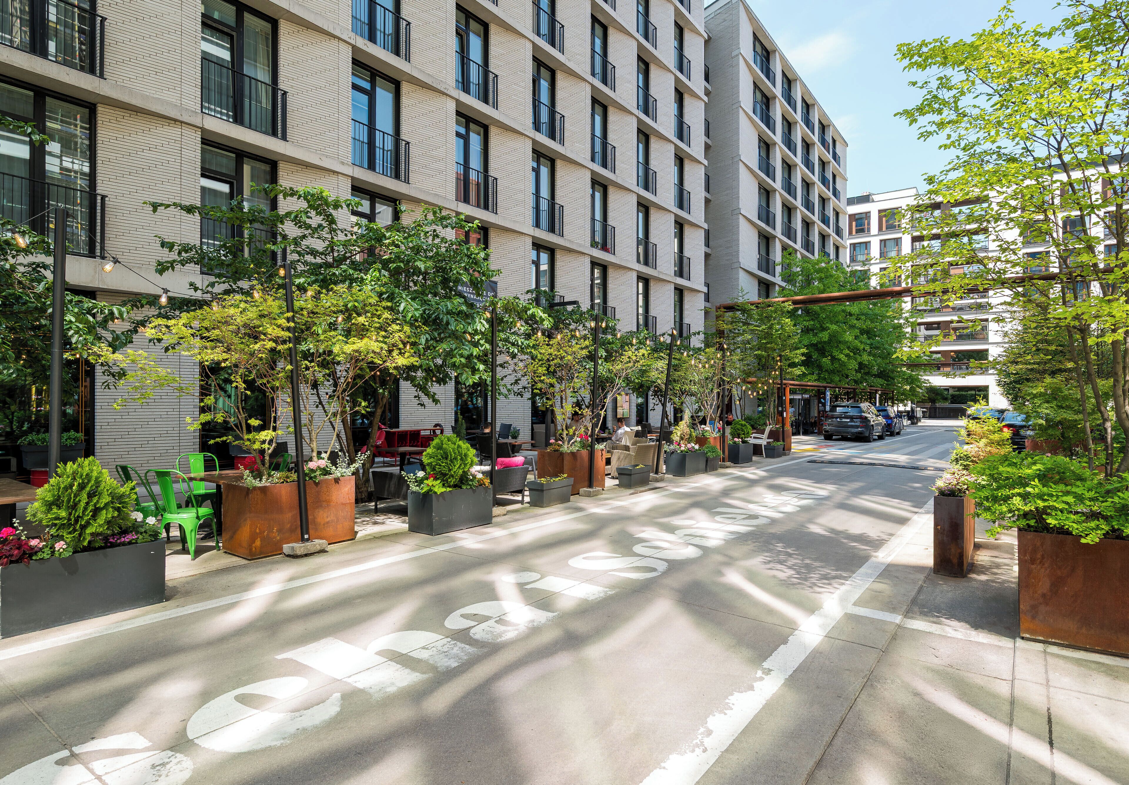 Une rue urbaine moderne, bordée de jardinières et agrémentée de sièges extérieurs le long du trottoir.