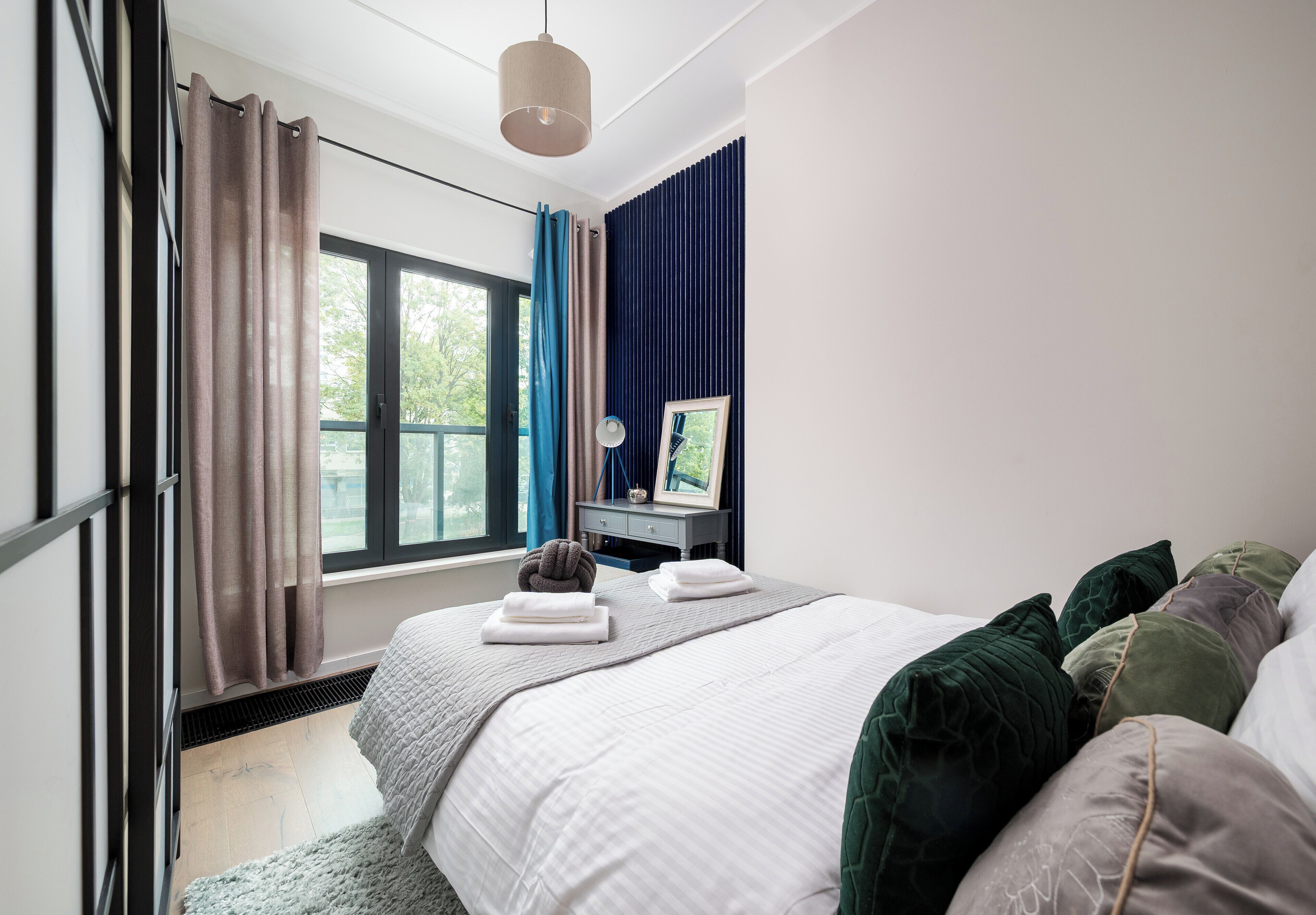 A bedroom with a bed, a desk, a window, and curtains.