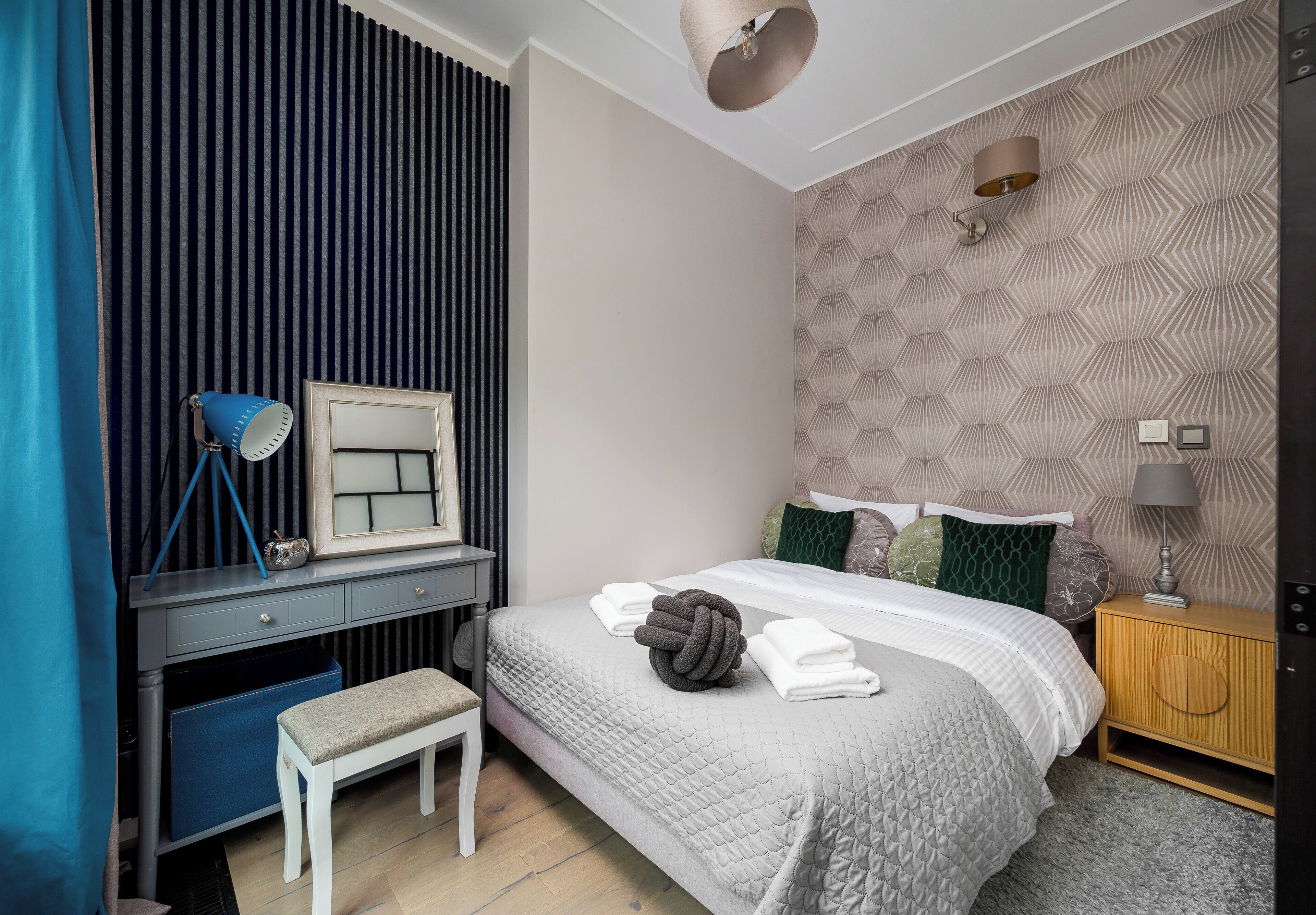 Ein Schlafzimmer mit einem Bett, Nachttisch, Bank, Kommode und einer Wand mit geometrischem Muster.