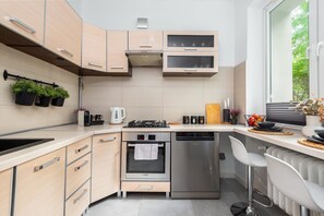 A modern kitchen with a built-in oven, dishwasher, and a window with a view of greenery. - Reymonta 34 Comfort Spot Studio (Katowice)