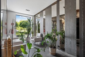 A modern lobby with a glass wall, indoor plants, and a view of the outdoors. - Północna White Elegance Apartment (Lublin)