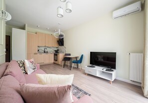 A modern living room with a sofa, a television, and a kitchen area with wooden cabinets and a dining table. - Westfield Mokotów Modern Apartment (Warszawa)