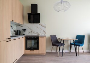 Una cocina moderna con horno empotrado, microondas y cafetera. Cuenta con un comedor con una mesa y dos sillas.