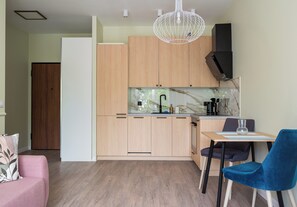 A modern kitchen with wooden cabinets, a marble countertop, and a dining area with a blue chair. - Westfield Mokotów Modern Apartment (Warszawa)