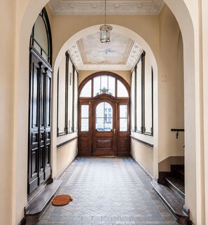 A hallway with a wooden door at the end, flanked by tall windows and a tiled floor. - Kopernika Old Town Homely Apartment (Poznań)