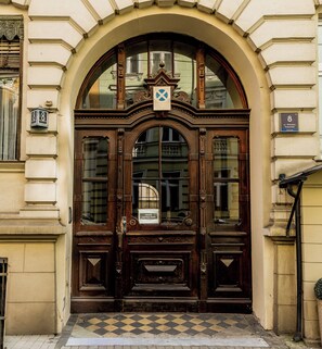 A historic building entrance with a large wooden door, a checkered floor, and a sign indicating a public space. - Kopernika Old Town Homely Apartment (Poznań)