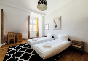 Hotellihuone, jossa on kaksi sänkyä, puinen työpöytä, tuoli, patteri ja taulu seinällä.