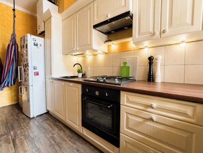 A kitchen with wooden cabinets, a stove, an oven, and a hanging rack. - Kopernika Old Town Homely Apartment (Poznań)