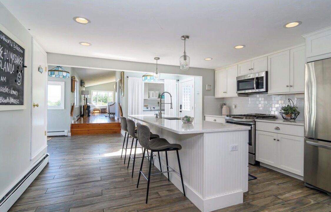A modern kitchen with a central island, bar stools, stainless steel appliances, and a bright, open layout.