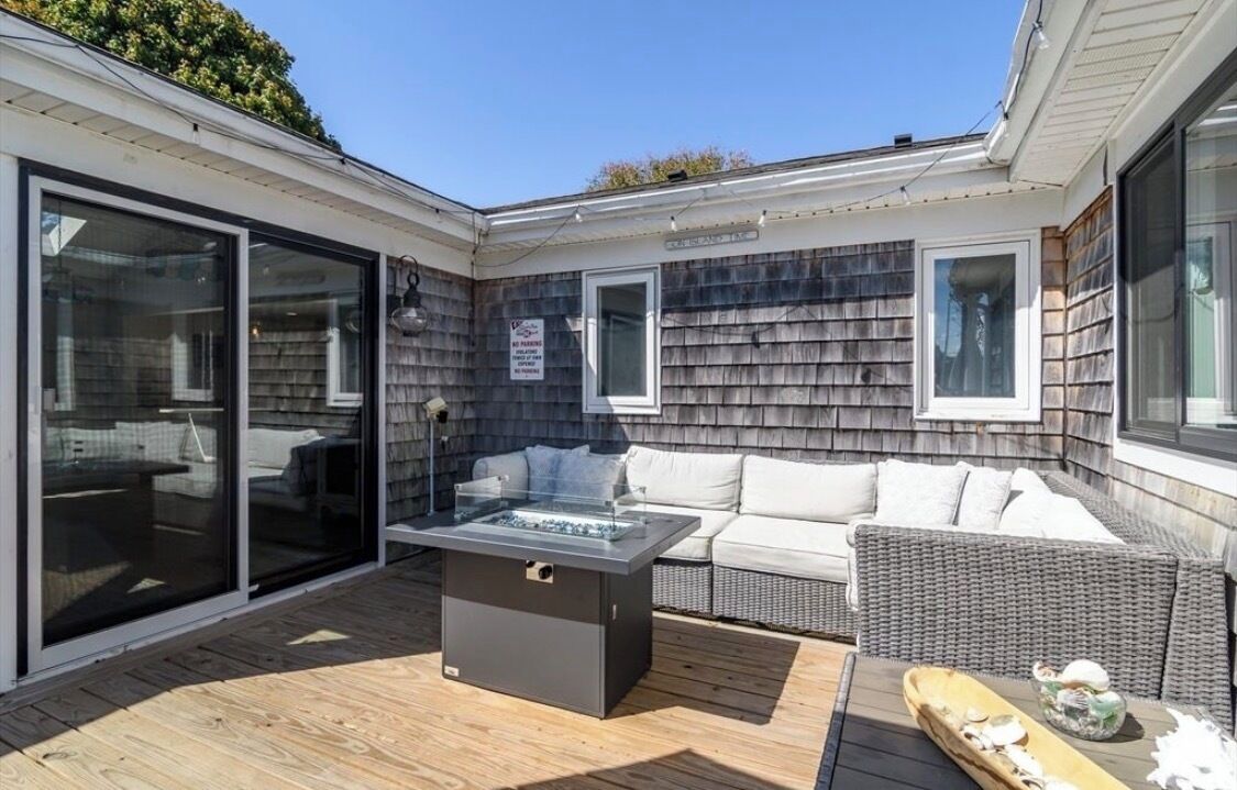 A patio with a glass-enclosed sliding door, a built-in fire pit, a wicker sofa, and a dining table.