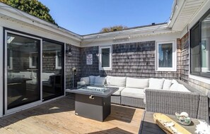 A patio with a glass-enclosed sliding door, a built-in fire pit, a wicker sofa, and a dining table. - 4-bedroom house on Mashnee Island Cape Cod feet away from amazing beaches (Bourne)
