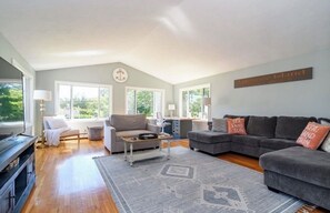 A spacious living room with a grey sofa set, a coffee table, and a large window providing natural light.