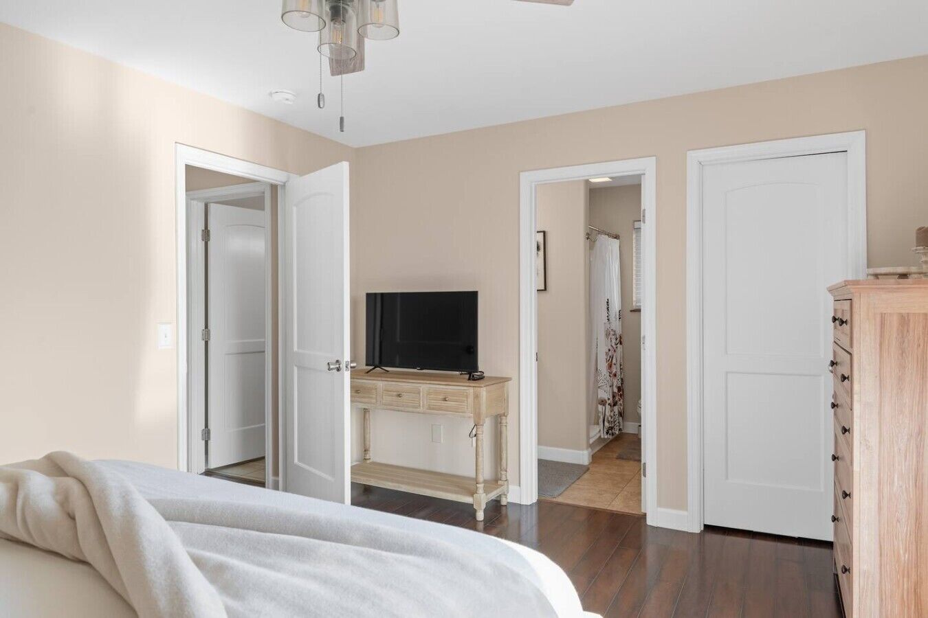 Ein Schlafzimmer mit einem Bett, einer Kommode, einem Fernseher auf einem Schrank und einem Flur, der in einen anderen Raum führt.