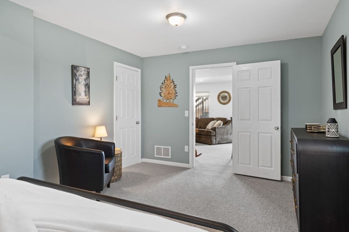 A bedroom with a bed, a chair, a desk, and a dresser. There is a door leading to another room.