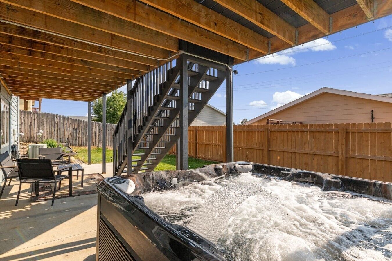 A hot tub with a wooden deck and a metal staircase leading to a covered area.