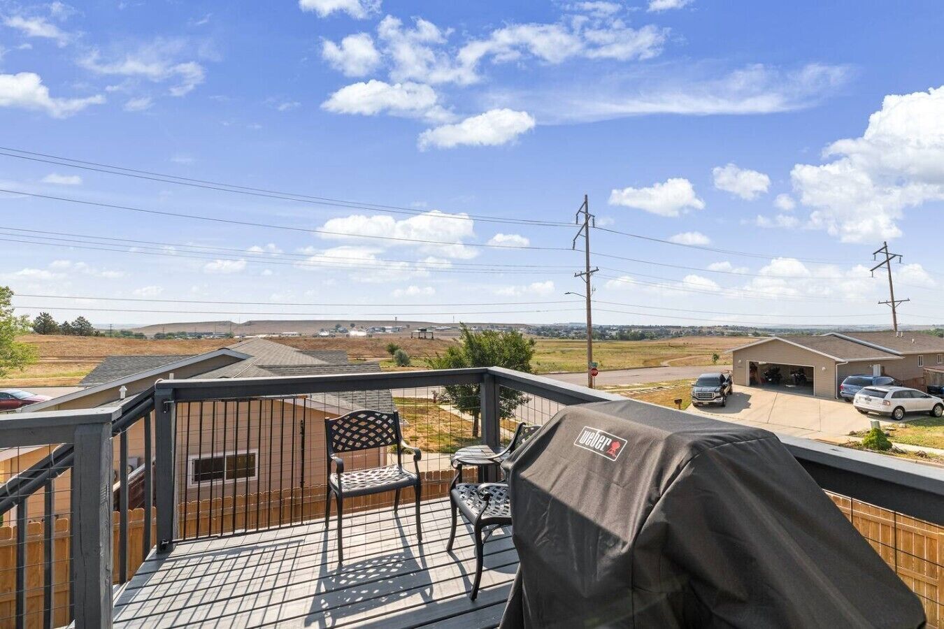 A balcony with a view of a residential area, a covered grill, and a chair.