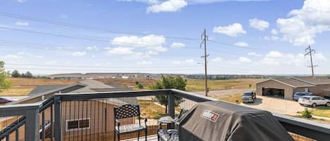 A balcony with a view of a residential area, a covered grill, and a chair.