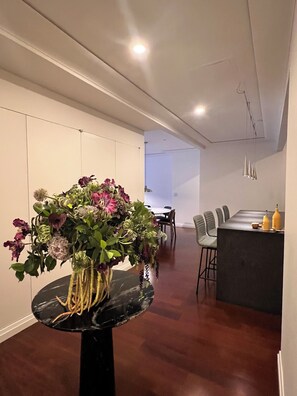 Un interior modern amb una zona de menjador, una taula de marbre negre i un centre de taula floral, i una barra amb dues ampolles grogues.