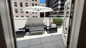 A balcony with a grey sofa, a small table, and a white umbrella. - Designer 1685 SF Penthouse, plus huge 650 SF terrace, looks to Trinity Church (New York)