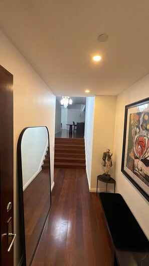 A hallway with a wooden floor leading to a staircase, a small table with a statue, and a framed painting on the wall. - Designer 1685 SF Penthouse, plus huge 650 SF terrace, looks to Trinity Church (New York)