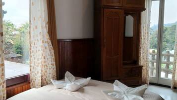 A hotel room with a bed, a wooden wardrobe, and a view of greenery through the window.