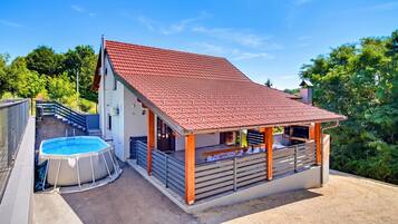 A two-story house with a red-tiled roof, a swimming pool, and a covered patio area.