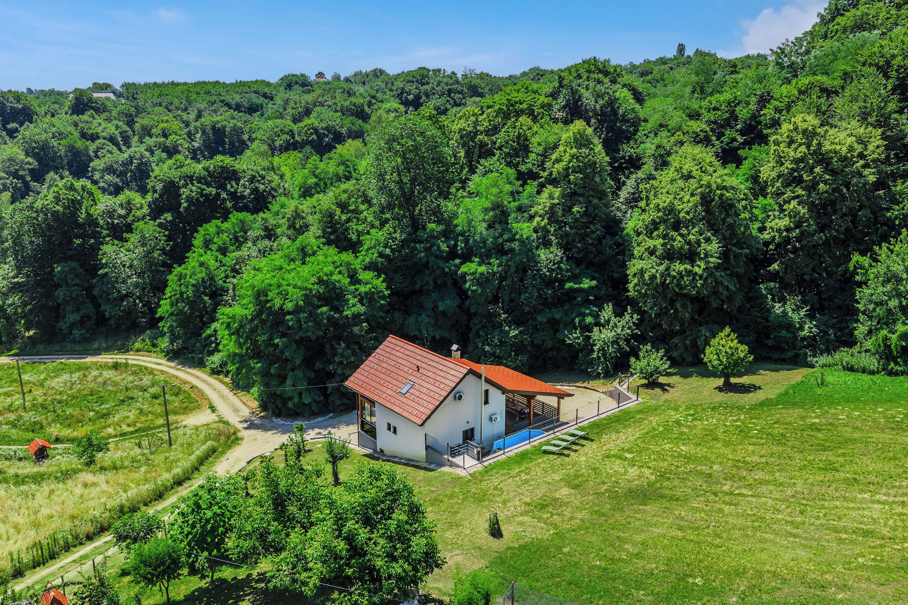 A modern house with a red roof, surrounded by lush greenery and a clear sky.