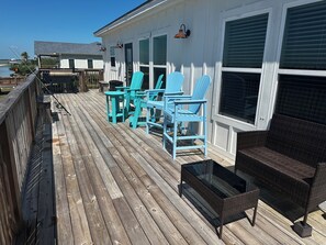 A wooden deck with outdoor furniture, including chairs and a table, overlooking a body of water. - Salt Lake Sunsets-Waterfront Home-Private Dock-Boat Parking-Stunning Sunsets (Rockport)
