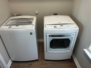 On aperçoit deux appareils électroménagers blancs, probablement un sèche-linge et une machine à laver, dans un coin, avec un plancher en bois et un mur à texture.
