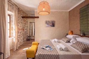 A bedroom with a stone wall, a bed with rolled towels, a magazine on the bed, a yellow chair, and a hanging light fixture. - Villa Dalmatia | Luxury Stone Villa with Pool & Tennis, Biograd na Moru, Croatia (Biograd na Moru)
