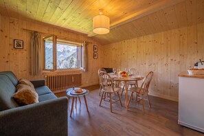 A cozy cabin interior with a dining area, a sofa, and a window with a mountain view. - Tapia - Mont Blanc View w/Parking, Near Charamillon Lift | 2BR, Sleeps 4, Le Tour (Argentière), France (Le Tour (Argentière))