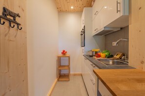 A compact kitchen with wooden cabinets, a stainless steel sink, and a small wooden shelf with fruit. - Tapia - Mont Blanc View w/Parking, Near Charamillon Lift | 2BR, Sleeps 4, Le Tour (Argentière), France (Le Tour (Argentière))