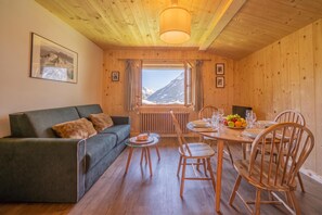 Une pièce chaleureuse avec un plafond en bois, un canapé, une table à manger avec des chaises et une fenêtre donnant sur les montagnes.
