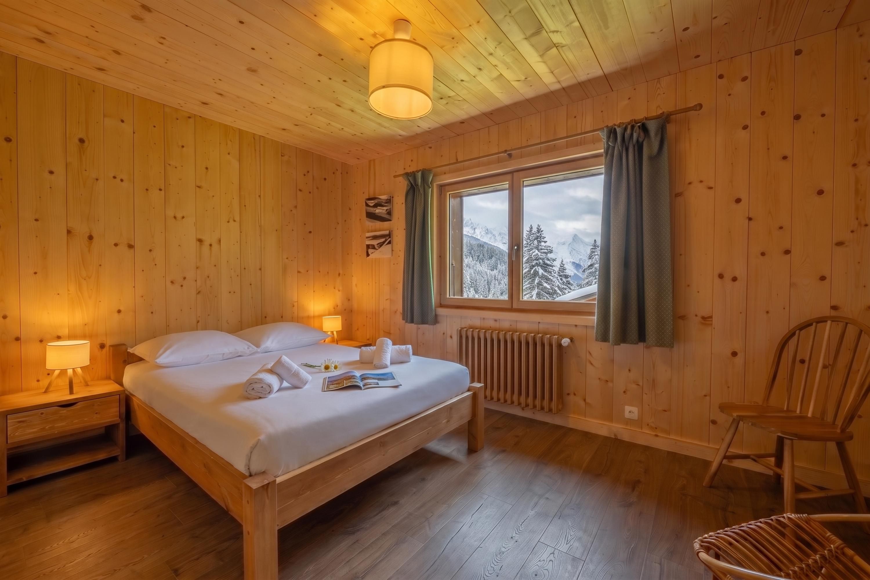 Un dormitorio de cabaña de madera con cama, lámparas de noche, ventana con cortinas, radiador y una silla.