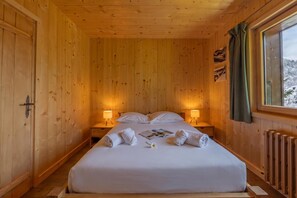A wooden cabin room with a bed, two bedside lamps, and a window with a view of snow-covered mountains. - Tapia - Mont Blanc View w/Parking, Near Charamillon Lift | 2BR, Sleeps 4, Le Tour (Argentière), France (Le Tour (Argentière))