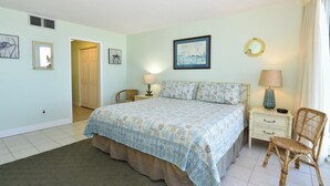 Ein Schlafzimmer mit einem Bett, zwei Nachttischen, einem Sessel, einer Tür und Wandbildern.