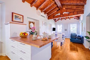 A modern kitchen with a wooden island, white cabinetry, and a dining area with a blue sofa. - Paul | Spacious Central Apart & Garage, Salò, Italy (Salò)