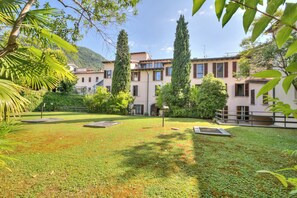 A courtyard with a lawn, trees, and a building with multiple windows and balconies. - Paul | Spacious Central Apart & Garage, Salò, Italy (Salò)