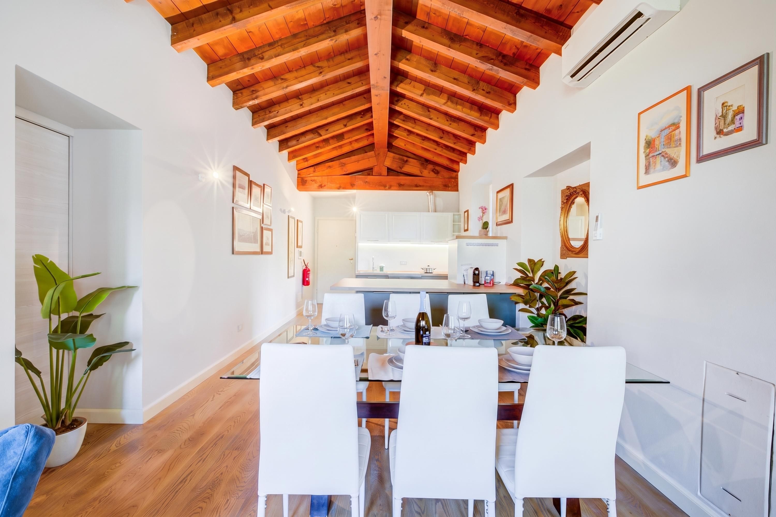 Un espace repas moderne avec un plafond en bois, des murs blancs et une cuisine en arrière-plan.